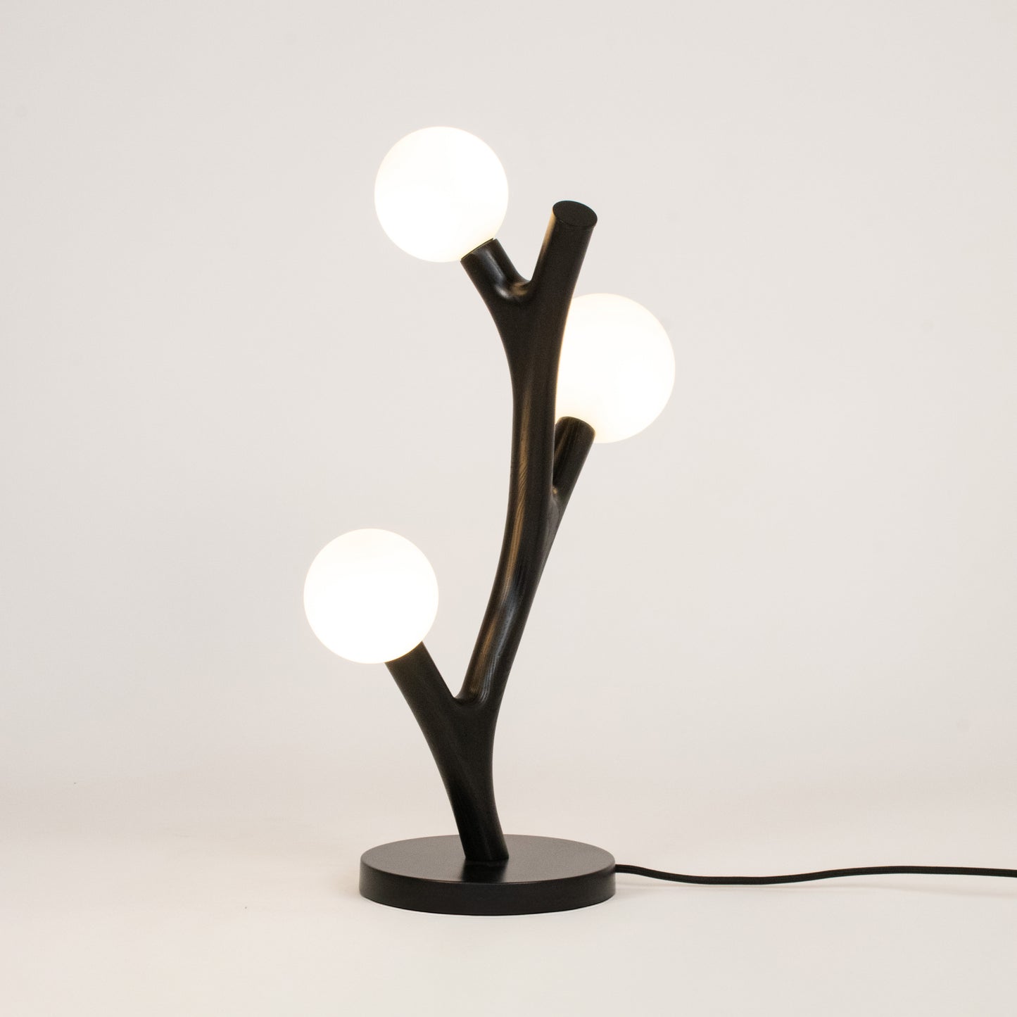 Modern table lamp with black branch-like design and three round lights on a white background