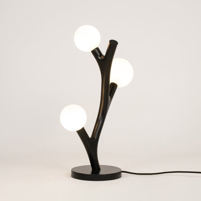 Modern table lamp with black branch-like design and three round lights on a white background