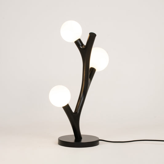 Modern table lamp with black branch-like design and three round lights on a white background