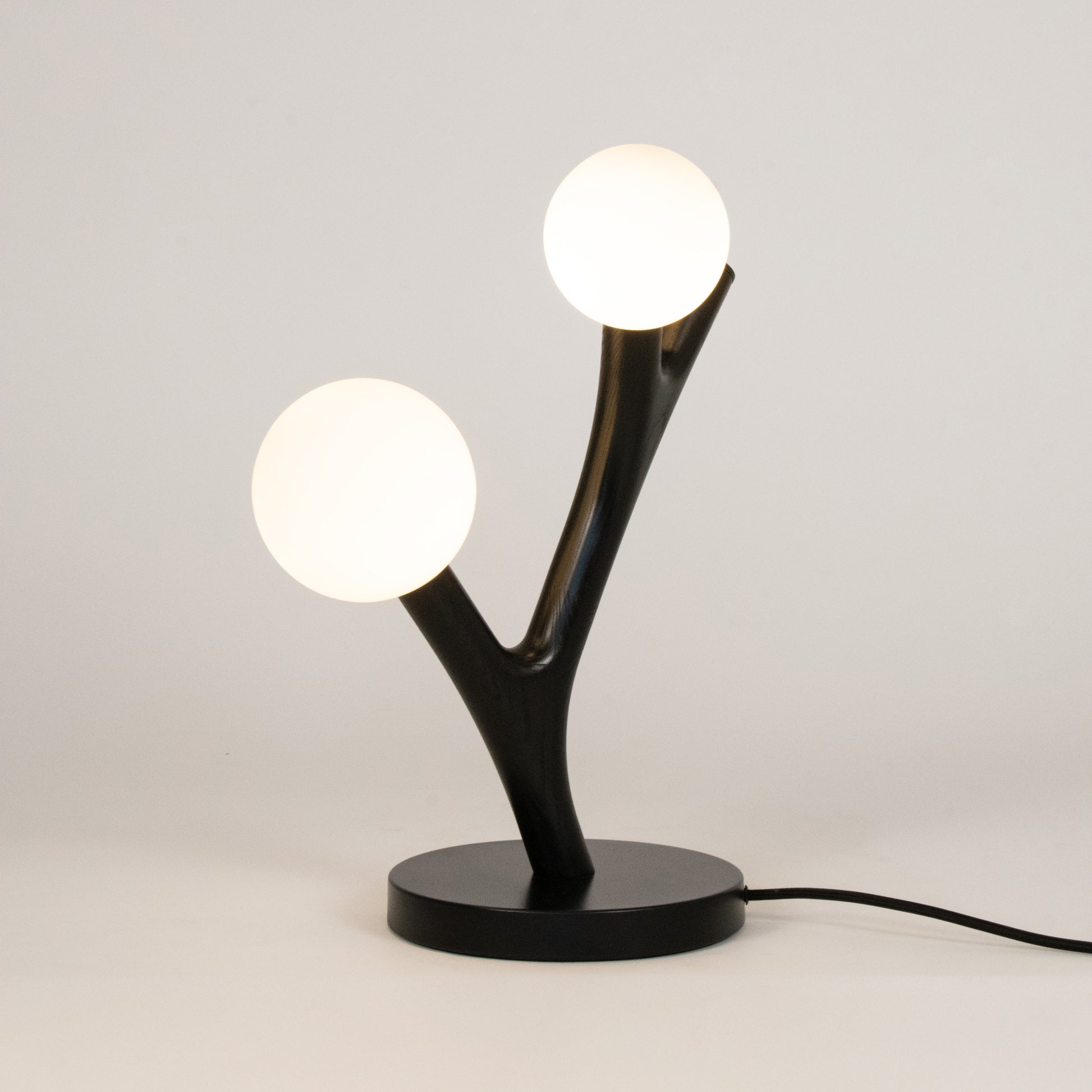 Modern table lamp with black base and two white spherical lights on a light gray background