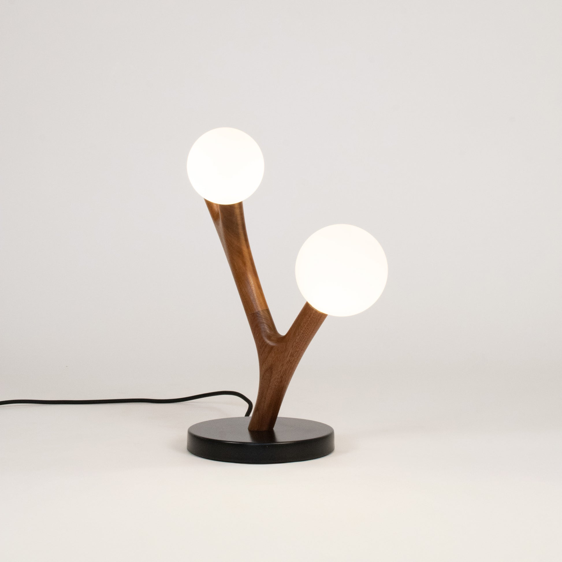 Table lamp with wooden branch design and two white bulbs on a light gray background