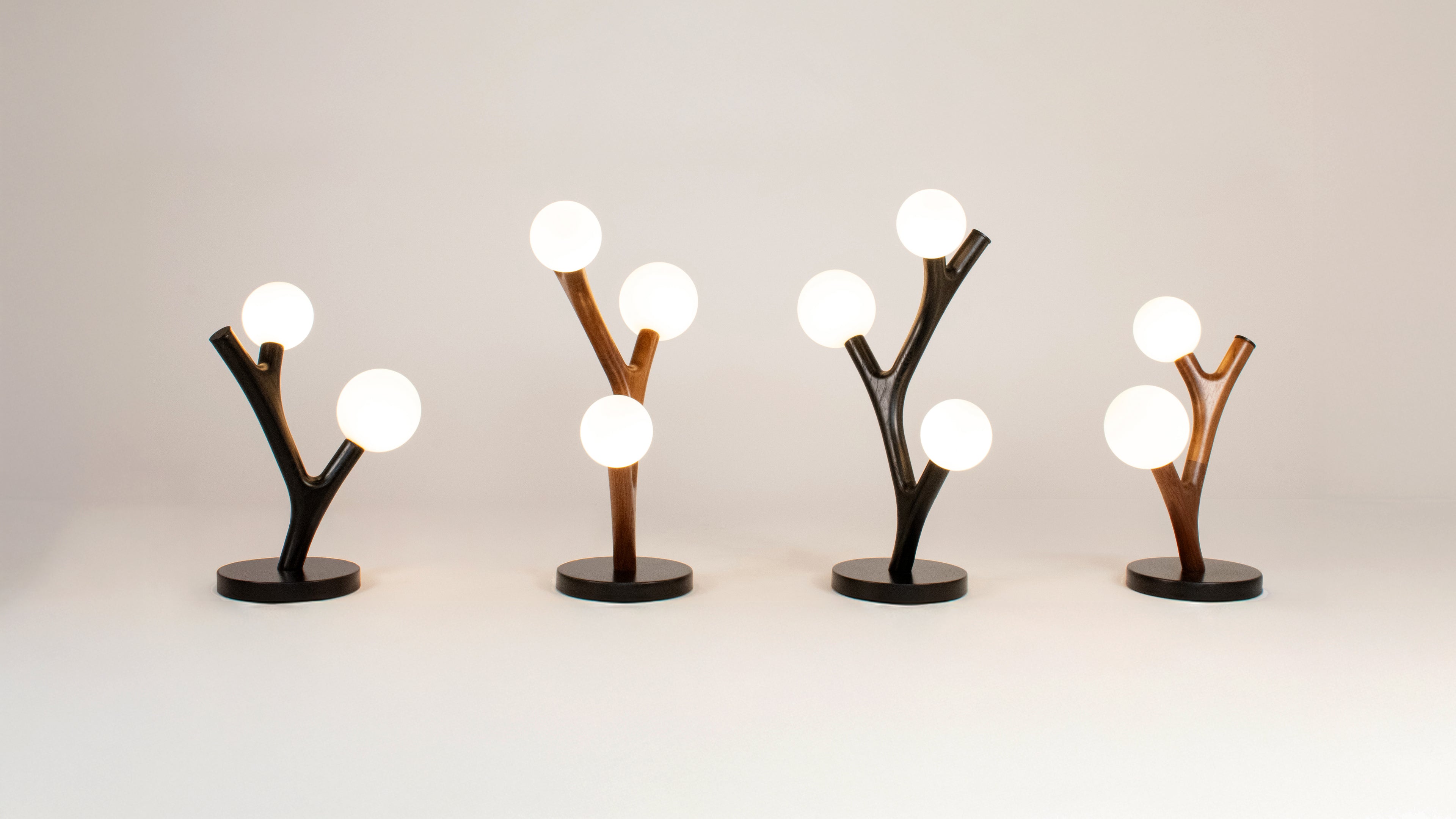 Four Chaparral modern table lamps with branch-like design on a plain background with various wood finishes